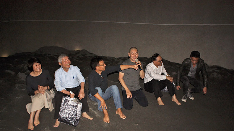 開幕當天,交通部部長賀陳旦(左二)在蔡明亮(右三)的導覽下一起坐在室內沙堆上。圖為東北角暨宜蘭海岸國家風景區管理處提供。