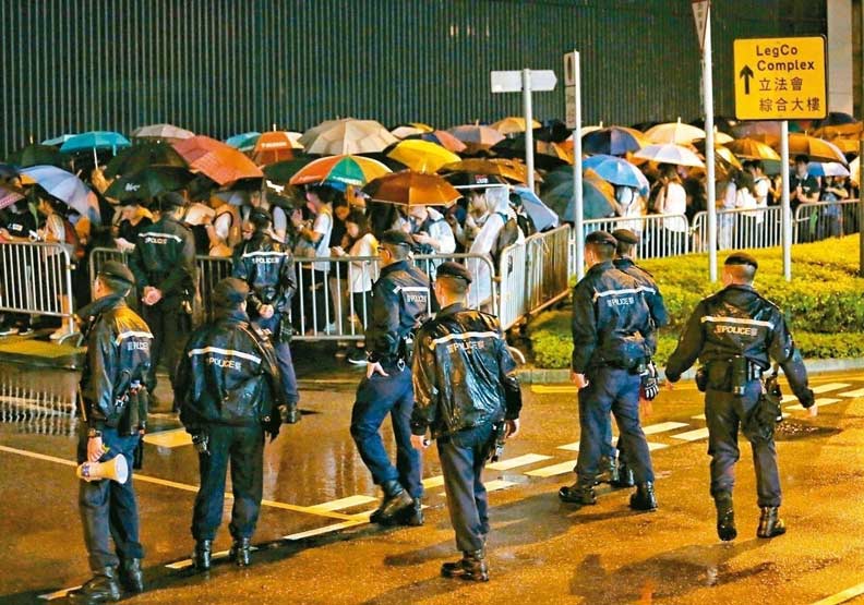 引發百萬港人上街抗議的「逃犯條例」修正草案，今將進行二讀辯論，香港民陣等團體發起包圍立法會和罷課、罷工、罷市，施壓港府撤回修例。昨晚立法會大樓前已有群眾聚集，現場警力持續增加戒備。