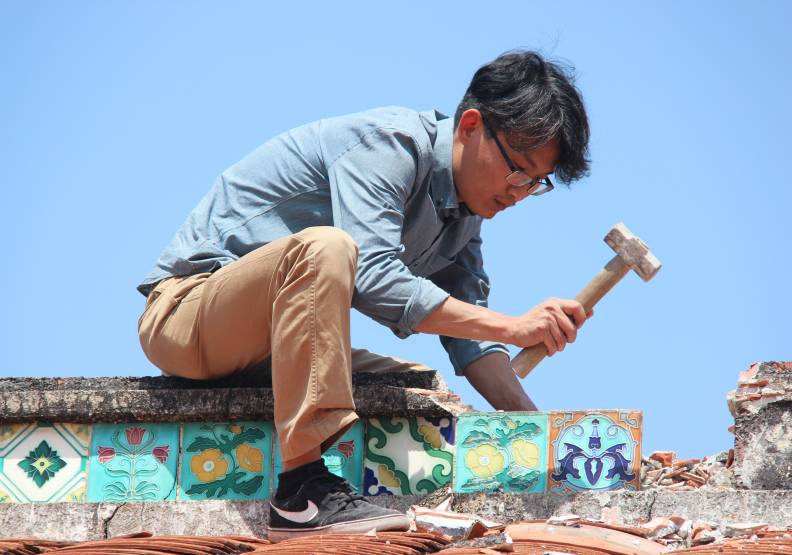 團隊搶救屏東馮安德家族「麒洛德源堂」花磚時，發現屋脊是空心，無法機器吊掛，徐嘉彬親自爬上屋頂，小心卸除花磚。徐嘉彬提供。