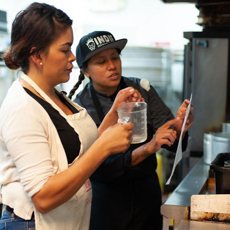 Food Shift 廚藝訓練導師 Suzy Medios(右)教導學徒用手頭容易取得的食物準備健康的餐點。來源:Food Shift Instagram