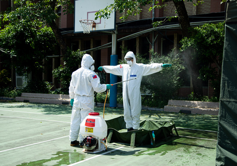 正在為夥伴消毒的防疫士，不難想像大熱天穿全套防護衣有多麼難耐。池孟諭攝