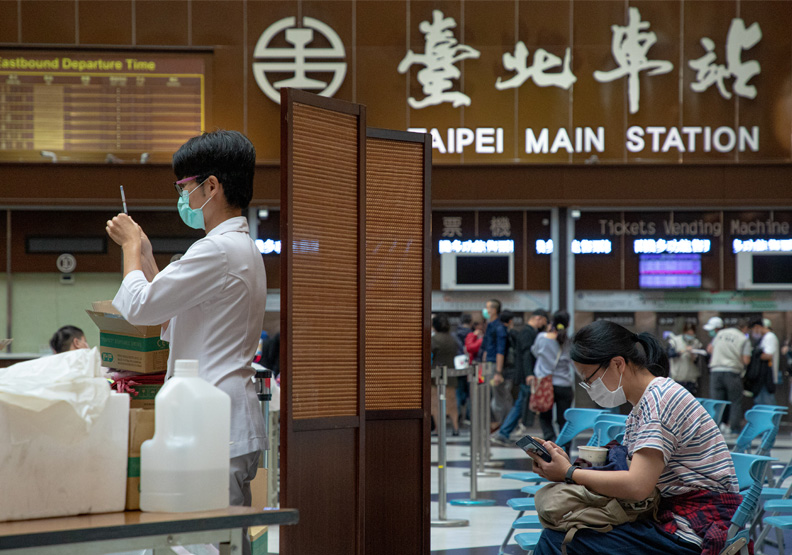 圖/台北車站疫苗接種站人潮踴躍,現場醫護人員忙著準備疫苗,屏風後方民眾滑著手機耐心等候叫號。池孟諭攝